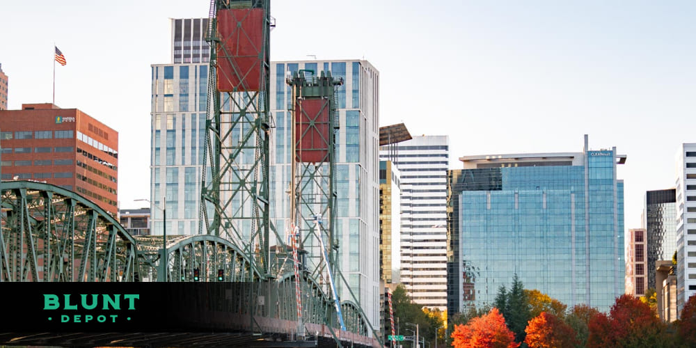 A person browsing the Blunt Depot cannabis delivery app on a smartphone, with the Portland bridge and skyline visible in the background.