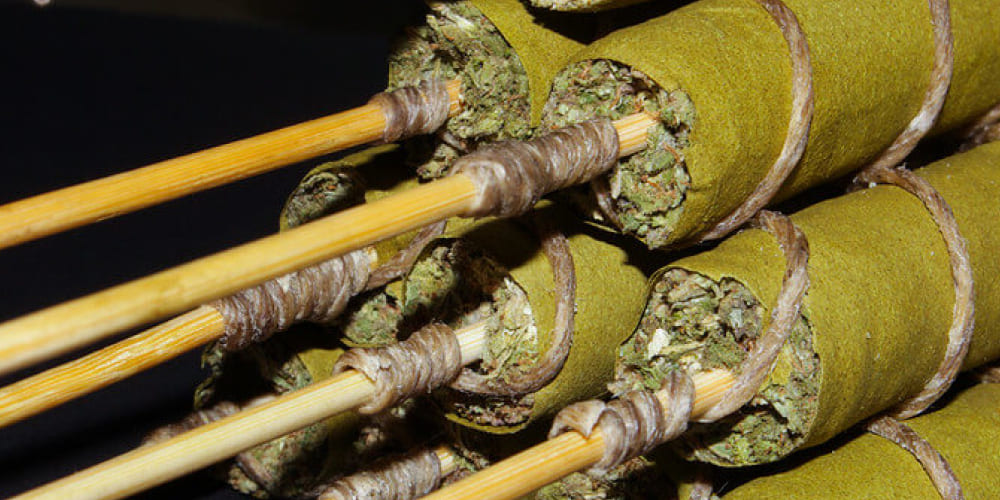 Step-by-step process of crafting a Thai Stick, from skewering buds to wrapping in cannabis leaves.