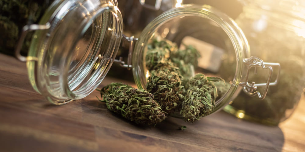 Open glass jar of THCA flower buds spilled onto a wooden table, with other jars in soft sunlight, showcasing quality THCA flower strain in San Antonio.