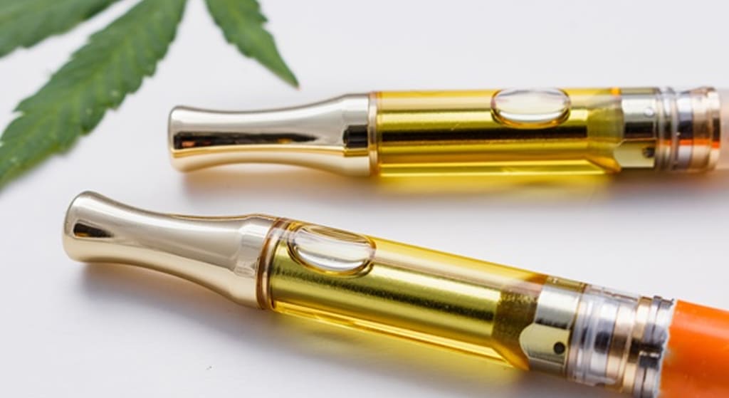 Two gold-tipped vape cartridges filled with golden oil and a cannabis leaf in the background.