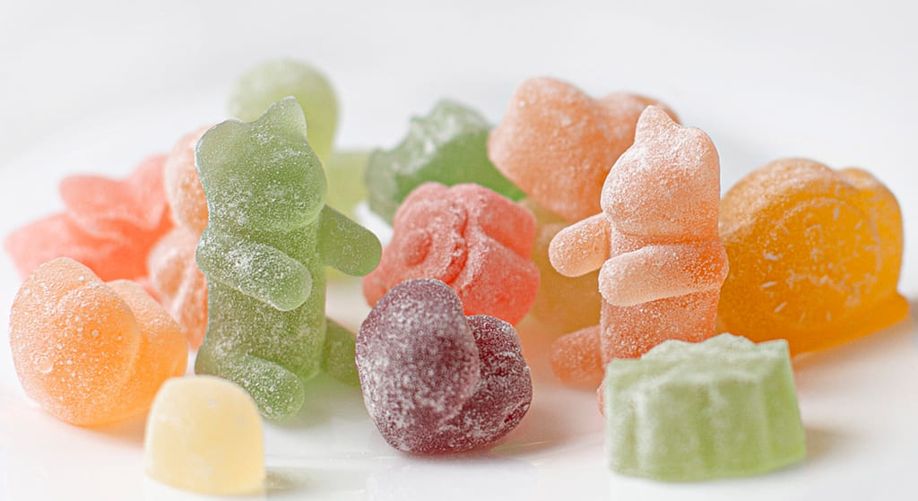 Assorted fruit-shaped gummies, lightly coated in sugar, on a white background.