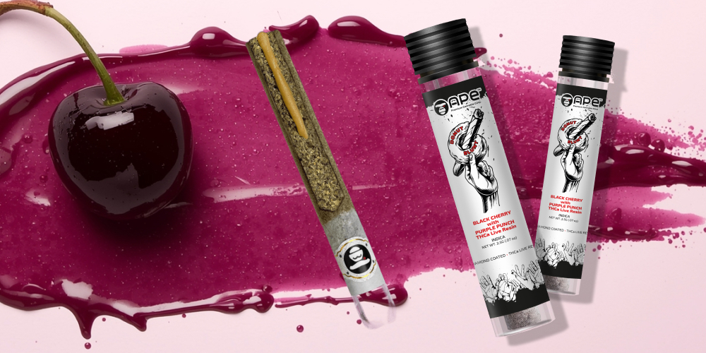 A single dark cherry with its stem sits on a splash of purple liquid, positioned next to a single pre-rolled blunt. Two product containers are shown on the right against a pale pink background.