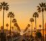 AI Generated Image: Hyper-realistic street-level photograph of a generic Southern California coastal city streetscape at golden hour, showing blank storefront facades, low-rise buildings, neutral street furniture, and distant hills under warm soft light