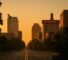 AI Generated Image: Hyper-realistic golden hour street-level view of Sacramento cityscape with clean storefronts, planter silhouette, and leading lines converging to center under soft warm light