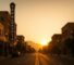 AI Generated Image: Hyper-realistic golden hour street-level view of San Bernardino city street with clean storefront reflections, low-rise buildings, neutral street furniture, and leading lines converging center under warm cinematic lighting.